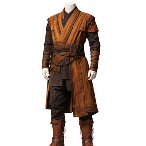 May include: A brown and black costume with a long coat, pants, and boots. The costume features a wrap-style top with a wide belt and intricate detailing. The sleeves and boots have a textured appearance, and the outfit is displayed on a mannequin.