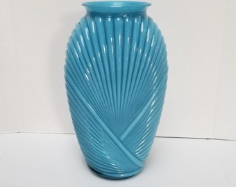 May include: A light blue glass vase with a fan-shaped design. The vase is tall and slender with a rounded base.