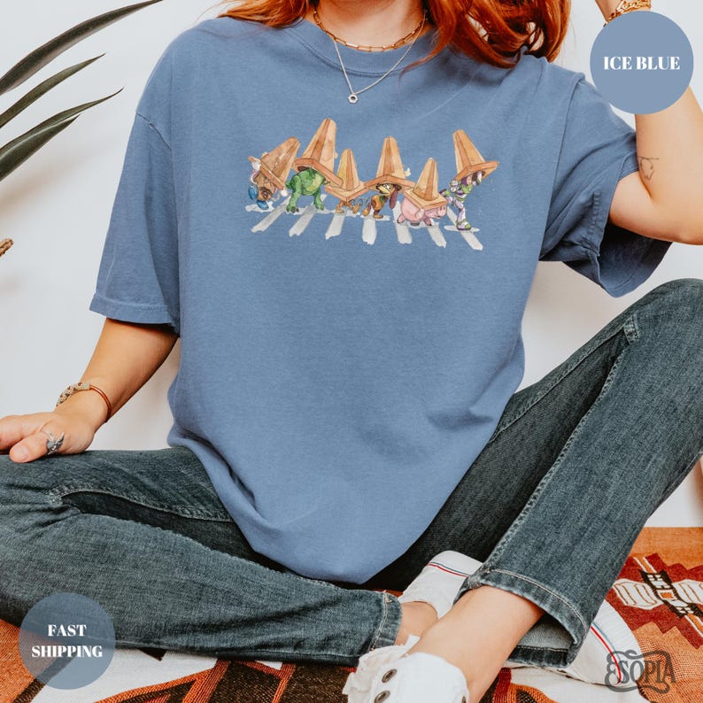 May include: Ice blue t-shirt featuring a graphic of cartoon characters crossing a crosswalk, wearing sombreros. The shirt is a light blue color. The text "ICE BLUE" is in a circle on the upper right. The text "FAST SHIPPING" is in a circle on the lower left.