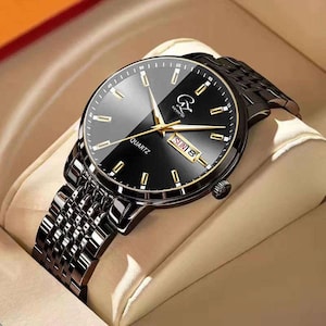 Può includere: Orologio al quarzo nero con cinturino in metallo nero. Il quadrante dell'orologio è nero con lancette e indicatori dorati. L'orologio mostra il giorno e la data. La parola "QUARTZ" è stampata sul quadrante.