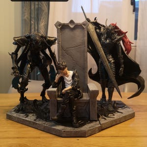 May include: A detailed figurine set, approximately 11.8 inches (30 cm) wide, featuring a central throne with a seated figure. Flanking the throne are two imposing, dark-colored figures, one with a large sword. The set is on a gray, geometric base.