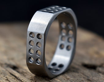 May include: A silver ring with a square design and a pattern of small holes. The ring is made of metal and has a brushed finish.