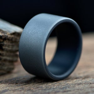 May include: A dark gray silicone ring with a matte finish. The ring is on a wooden surface.