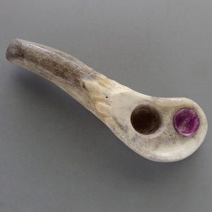 May include: A smoking pipe crafted from a textured, off-white antler segment. The bowl features a circular metal mesh screen insert, and a small, polished, circular magenta stone inlay is embedded into the flat surface near the bowl opening.