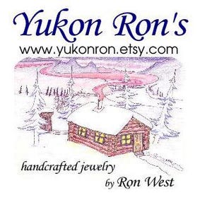 Peut inclure: Un logo avec le texte Yukon Ron's, www.yukonron.etsy.com, handcrafted jewelry, et by Ron West. L'illustration montre une cabane en rondins marron avec un toit enneigé, des fenêtres jaunes et une cheminée dégageant de la fumée dans un paysage.