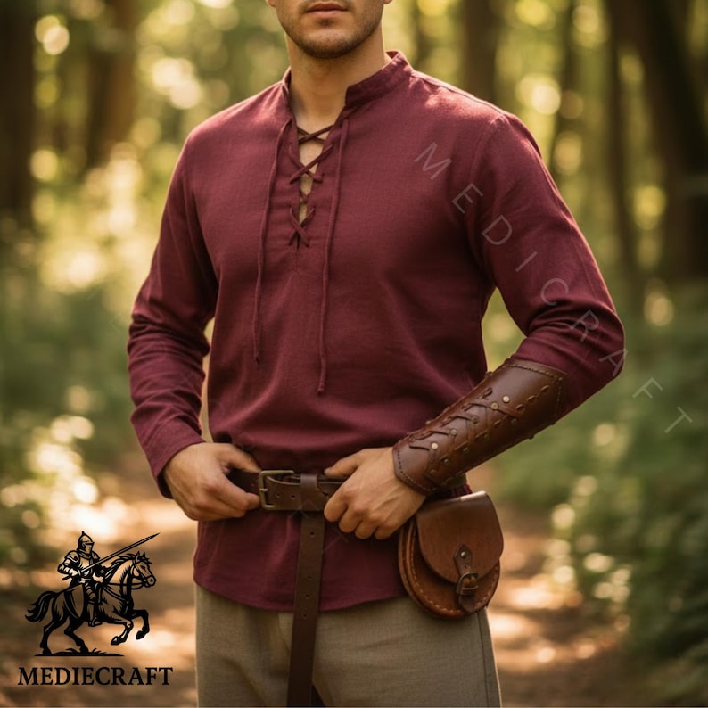 May include: A burgundy long-sleeve shirt with a lace-up neckline, brown leather belt, pouch, and arm guard. The image features the "MEDIECRAFT" logo. The shirt is made of a soft, comfortable material. The outfit has a medieval theme.