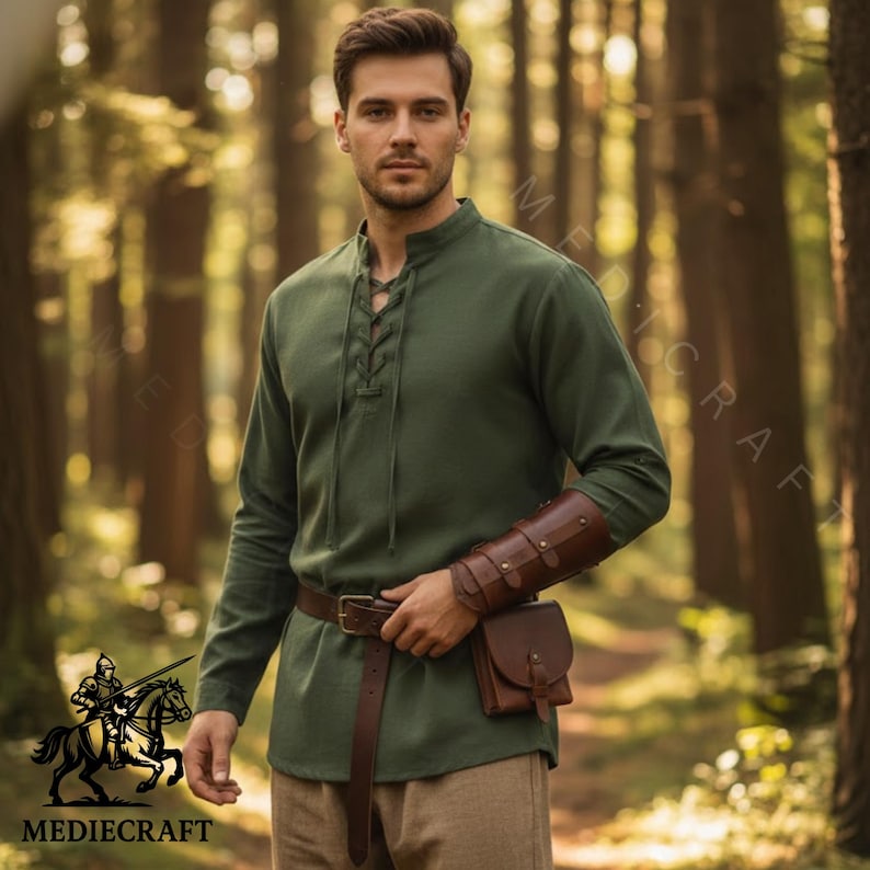 May include: A green long-sleeved tunic with a lace-up neckline, brown leather belt, and matching pouch. The image also shows a brown leather arm guard. The Mediecraft logo is visible in the lower left corner.