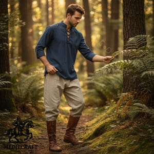 May include: A navy blue linen shirt with a lace-up neckline and three-quarter sleeves, worn with light beige linen trousers and brown leather boots. Ideal for historical events or themed occasions.