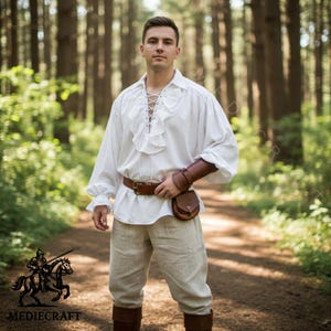 Man wearing white medieval ruffle shirt with lace up front, renaissance fair pirate style cotton tunic in forest setting.