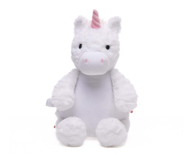 A white plush unicorn toy with a pink horn and tail sits against a white background.