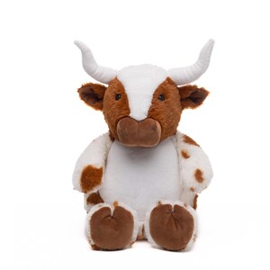 A stuffed toy cow with white horns and brown spots sits against a white background.