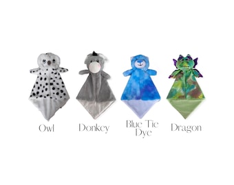 May include: Four plush security blankets featuring animal heads: a white and black spotted owl, a gray donkey, a blue tie-dye bear, and a green and purple dragon. Each blanket has a soft, triangular body and is labeled Owl, Donkey, Blue Tic Dye, Dragon.