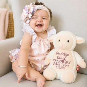 May include: A plush cream-colored lamb toy featuring embroidered text that reads Madelyn Dawn, 7 lbs 8 oz, 20.5 inches, 11:23 pm, and 8.12.2023, with a small red tag on the side and a heart icon between the weight and length measurements.