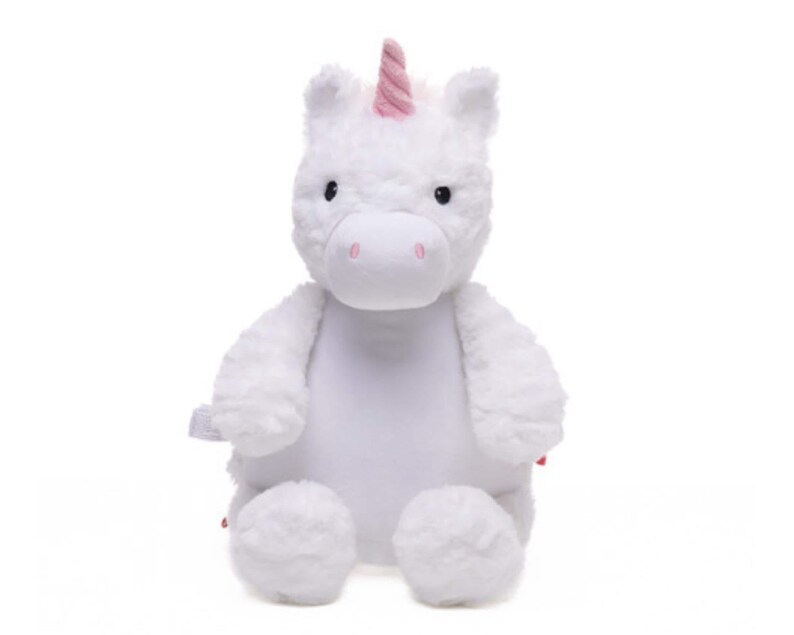 A white plush unicorn toy with a pink horn and tail sits against a white background.