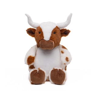 A stuffed toy cow with white horns and brown spots sits against a white background.
