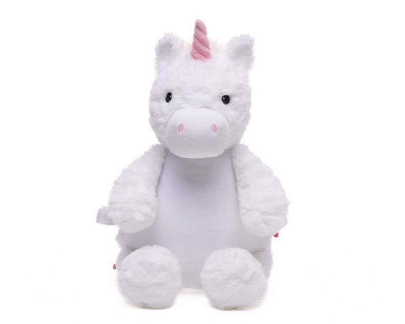 A white plush unicorn toy with a pink horn and tail sits against a white background.