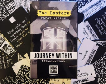 May include: A tarot oracle deck titled "The Lantern" with a black and white illustration of a lantern. The deck is surrounded by other cards with text and illustrations. The words "Journey Within" are visible.