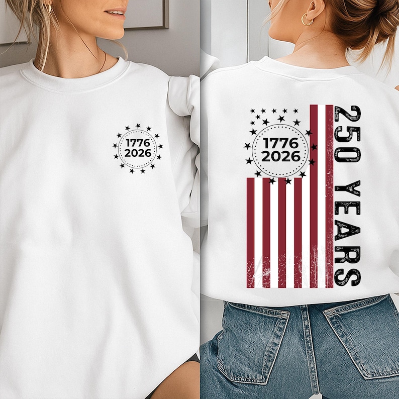 May include: White sweatshirt with a graphic design. The front features a circular design with the text "1776 2026" surrounded by stars. The back displays a stylized American flag with the text "250 YEARS".