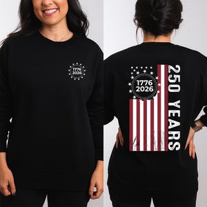 May include: Black sweatshirt with a white graphic on the front that says "1776 2026" inside a circle of stars. The back features a vertical American flag design with the text "250 YEARS".