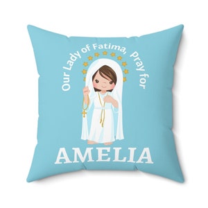 May include: A light blue throw pillow with a white image of Our Lady of Fatima praying for Amelia. The image is surrounded by a circle of gold stars.