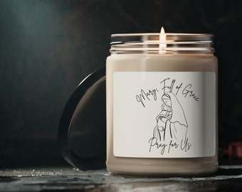 May include: A beige candle with a white label featuring a line drawing of Mary holding baby Jesus. The label reads "Mary, Full of Grace, Pray for Us."