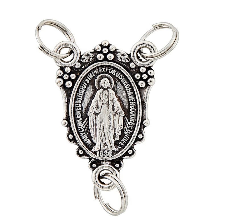 May include: A silver-coloured religious medal with three key rings. The oval-shaped medal features an image of a religious figure and the text "MARY COKCEIVED WITHOUT SIN PRAY FOR US WHO HAVE RECOURSE TO THEE" and the year "1830".