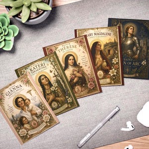 Pode incluir: Quatro cartões retangulares com ilustrações religiosas de Santa Gianna Beretta Molla, Santa Kateri Tekakwitha, Santa Teresinha do Menino Jesus, Santa Maria Madalena e Santa Joana d'Arc, com bordas florais ornamentadas e nomes impressos.