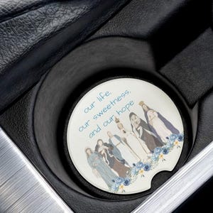 May include: White car coaster with a blue floral design and the text "our life, our sweetness, and our hope". The design features a group of women in blue robes with crowns and halos.
