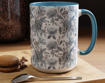 May include: A white ceramic mug with a blue rim and handle. The mug features a repeating pattern of blue watercolor flowers and crowns.