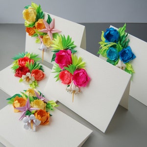 May include: Five handmade greeting cards with origami flowers. The cards feature different colored flowers, including pink, red, orange, yellow, and blue. Each card has a white background and is folded in half.