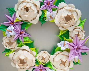 May include: A white origami paper flower wreath with purple and white flowers and green leaves.