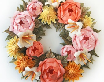 May include: A handmade origami wreath featuring a variety of paper flowers in shades of pink, peach, yellow, and white. The wreath includes detailed paper leaves and is arranged in a circular shape, perfect for home decor.