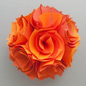May include: A close-up of an origami flower made from orange paper. The flower is made up of several layers of paper, creating a three-dimensional effect.