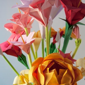 May include: A bouquet of origami flowers in a vase. The flowers are made of paper and are in shades of pink, red, and orange. The flowers are arranged in a vase and are a beautiful example of the art of origami.