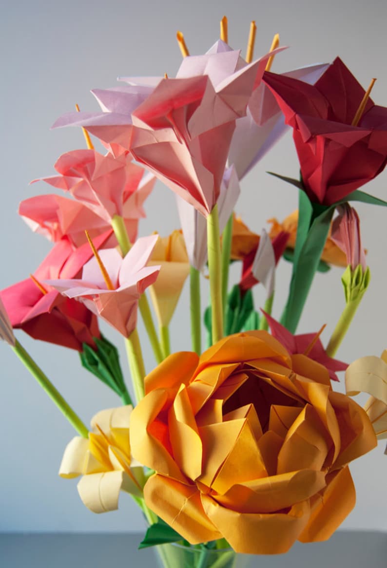 May include: A bouquet of origami flowers in a vase. The flowers are made of paper and are in shades of pink, red, and orange. The flowers are arranged in a vase and are a beautiful example of the art of origami.