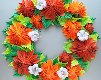 May include: A wreath made of orange and green origami paper flowers. The flowers are arranged in a circle and have a white center. The wreath is perfect for a spring or summer decoration.