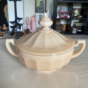 Puede incluir: Un azucarero vintage de vidrio de color crema con tapa y dos asas. El taz&oacute;n tiene un dise&ntilde;o acanalado y una perilla en la tapa.