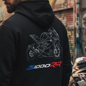 以下が含まれることがあります： 背面にスポーツバイクの白い線画グラフィックが施された黒いフード付きスウェットシャツ。バイクのイラストの下には、青と赤の文字でS1000RRというテキストがプリントされています。このパーカーは長袖でフードが付いています。