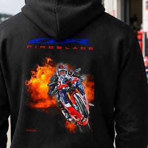 May include: A black hooded sweatshirt featuring a graphic on the back. The design displays the blue text CBR and red text FIREBLADE above an illustration of a rider on a red, white, and blue motorcycle surrounded by bright orange flames.