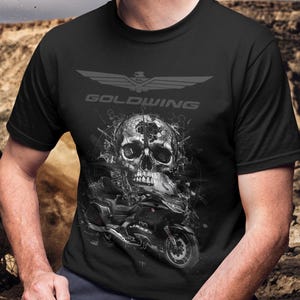 Könnte beinhalten: Schwarzes T-Shirt mit einem grafischen Design eines Schädels und eines Motorrads. Das Wort "GOLDWING" ist über dem Schädel aufgedruckt. Das Design ist in Grau- und Schwarztönen gehalten.