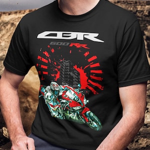 May include: Black t-shirt featuring a graphic of a red and white motorcycle with the text "CBR 600RR" in white. The design includes red radial lines and a cityscape silhouette, creating a dynamic visual.