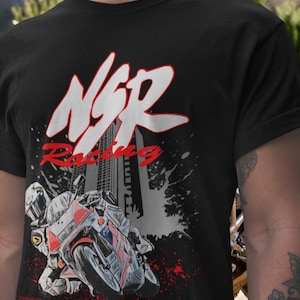 May include: Black t-shirt featuring a motorcycle racing design. The graphic includes the text "NSR Racing" in white and red, with a stylized image of a racer on a motorcycle. The design has a vintage, comic book style.