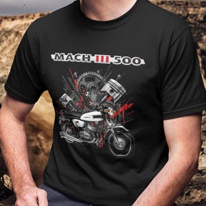 Może przedstawiać: Czarna koszulka z grafiką motocykla i napisem "MACH III 500". Projekt zawiera tłoki, koła zębate i czerwone plamy. Motocykl jest biało-czarny.