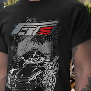 May include: Black t-shirt featuring a graphic of a three-wheeled vehicle. The shirt has a distressed design with the text "F3S" in a stylized font, with the "S" in red. The vehicle graphic is in black and white.