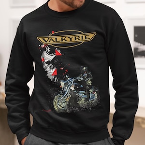 Puede incluir: Sudadera negra de cuello redondo con un gráfico de motocicleta. El gráfico presenta un motociclista en una moto, una calavera y la palabra "VALKYRIE" en letras doradas. El diseño tiene un aspecto vintage y desgastado.