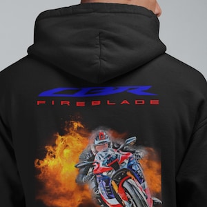 May include: Black hoodie featuring a motorcycle graphic with flames and the text "CBR FIREBLADE" in blue and red. The image shows a person riding a red, white, and blue motorcycle. The hoodie has a hood and a relaxed fit.