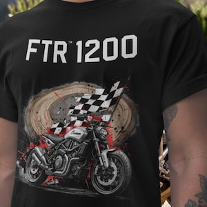 May include: Black t-shirt featuring the text "FTR 1200" in white. The shirt has a graphic of a motorcycle with a checkered flag, set against a wood-grain background with red paint splatter.