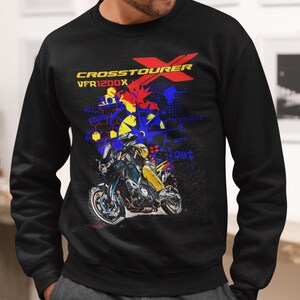 Könnte beinhalten: Schwarzes Sweatshirt mit Motorradgrafik und dem Text "CROSSTOURER VFR1200X". Das Design enthält rote, gelbe und blaue Akzente. Getragen von einer Person mit grauer Kappe.