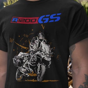 Peut inclure: T-shirt noir avec un motif de moto et le texte "R1200 GS" en rouge et bleu. Le design comprend un motard sur une moto avec une rose des vents. Le t-shirt est fait d'une matière douce.