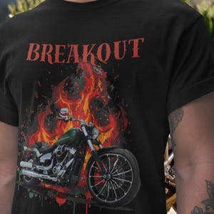 May include: Black t-shirt featuring the word "BREAKOUT" in red above a motorcycle graphic. The motorcycle is green and silver, set against a backdrop of flames in red, orange, and yellow.